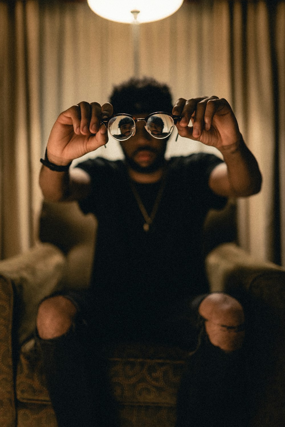 a man sitting on a couch holding up his glasses