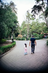 A father and child holding hands, walking through a sunlit park.