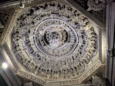 A detailed view of an intricately carved stone ceiling with concentric circular patterns featuring ornate designs and numerous small sculptures. The artwork demonstrates a high level of craftsmanship and attention to detail, with symmetrical arrangements and elaborate motifs.