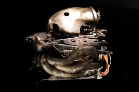 A high-performance car engine featuring intricate carbon fiber components and metallic parts is set against a dark background. The engine's design is modern and aerodynamic, showcasing exposed wiring and tubes.