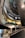Interior view of a modern, multi-level showroom with sleek architectural design elements. A green sports car is prominently displayed on a raised white platform, surrounded by floors displaying other vehicles. The overhead lighting and spiral design contribute to a futuristic ambiance.