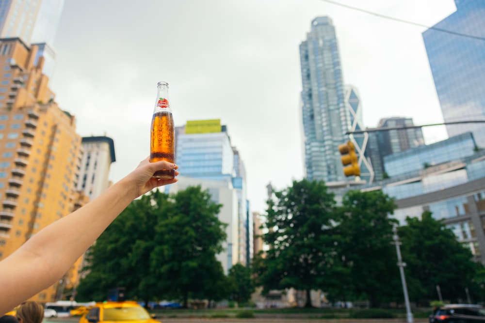 a person holding up a bottle of beer in a city