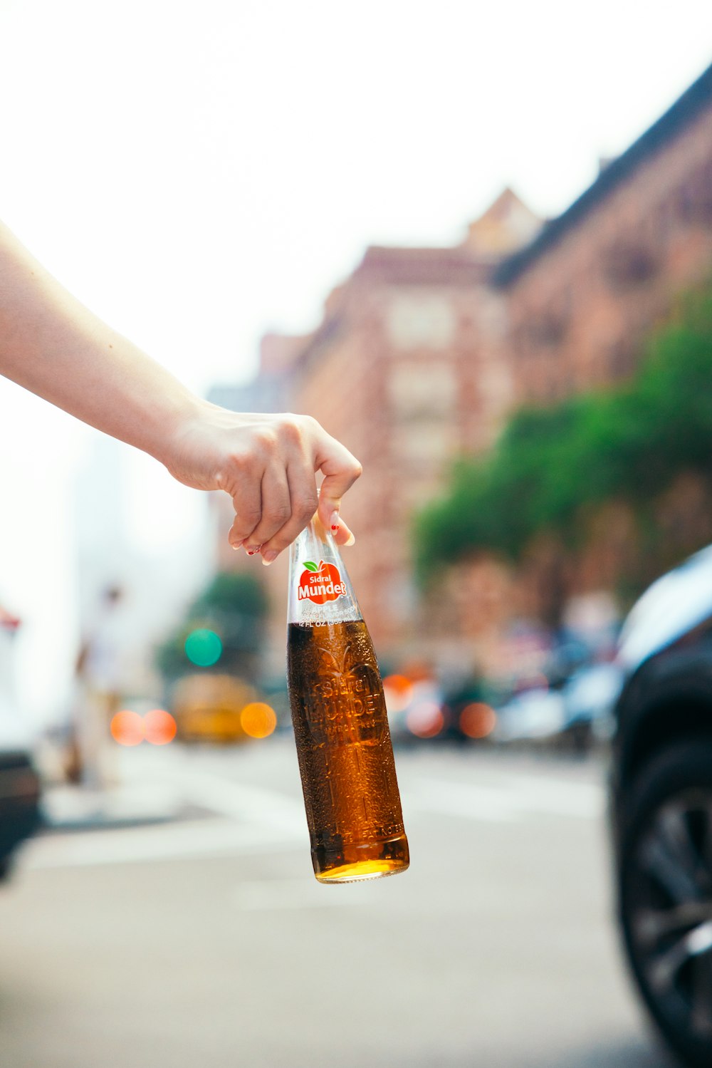 una persona che tiene una bottiglia di birra in una strada della città