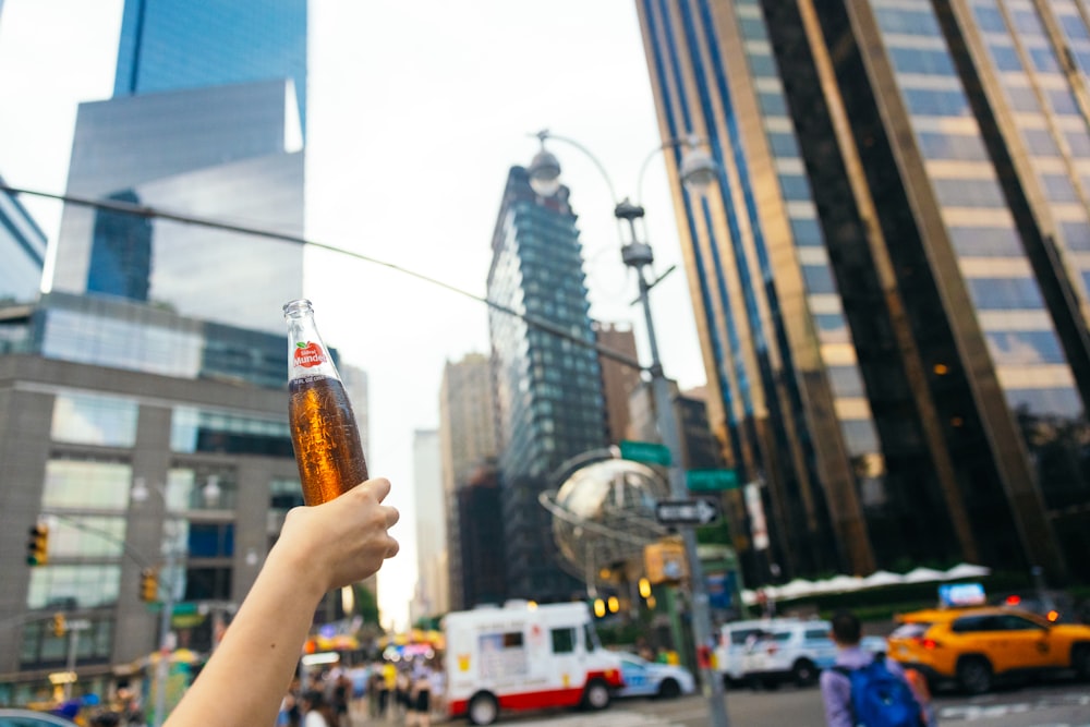 una persona che tiene in mano una bottiglia di birra in una città