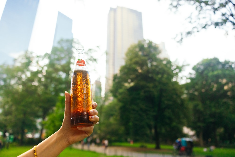 a person holding up a beer in a park