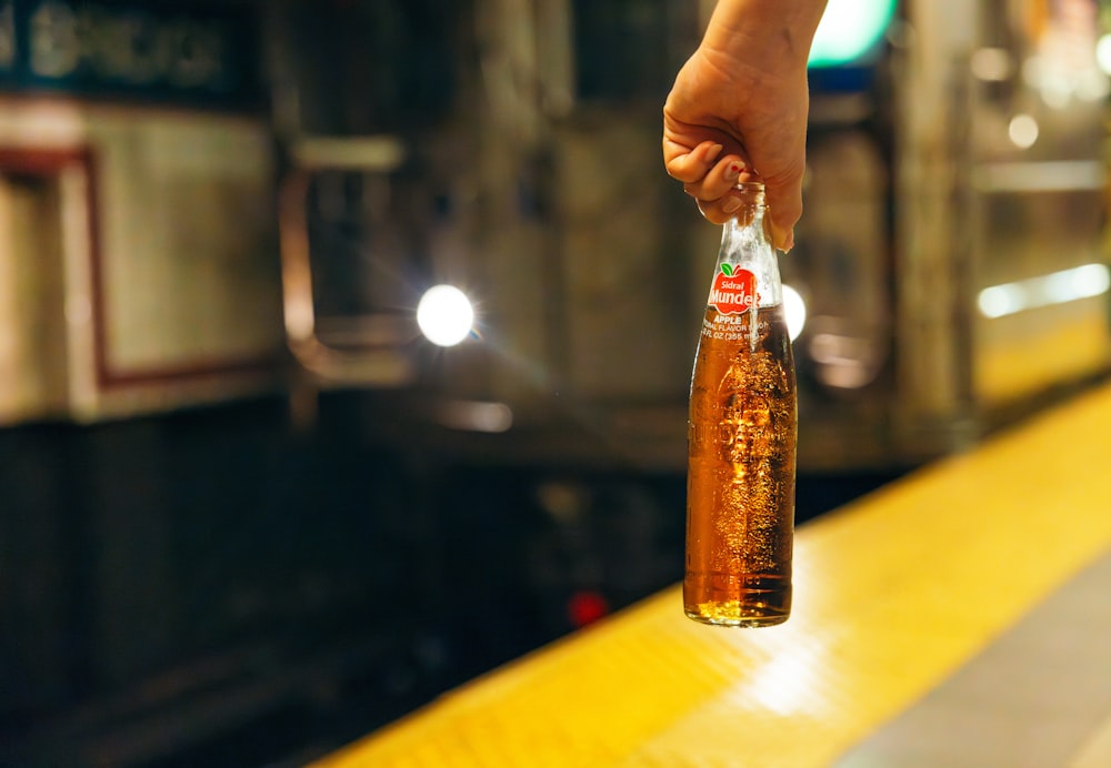 a person holding a bottle of beer on a train platform