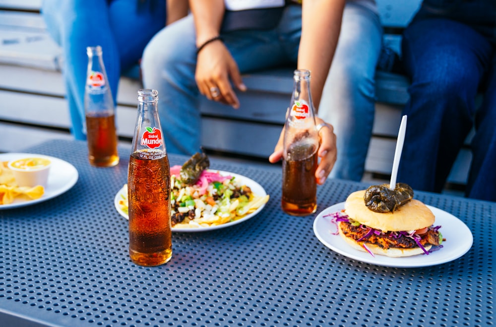 a table topped with plates of food and bottles of soda