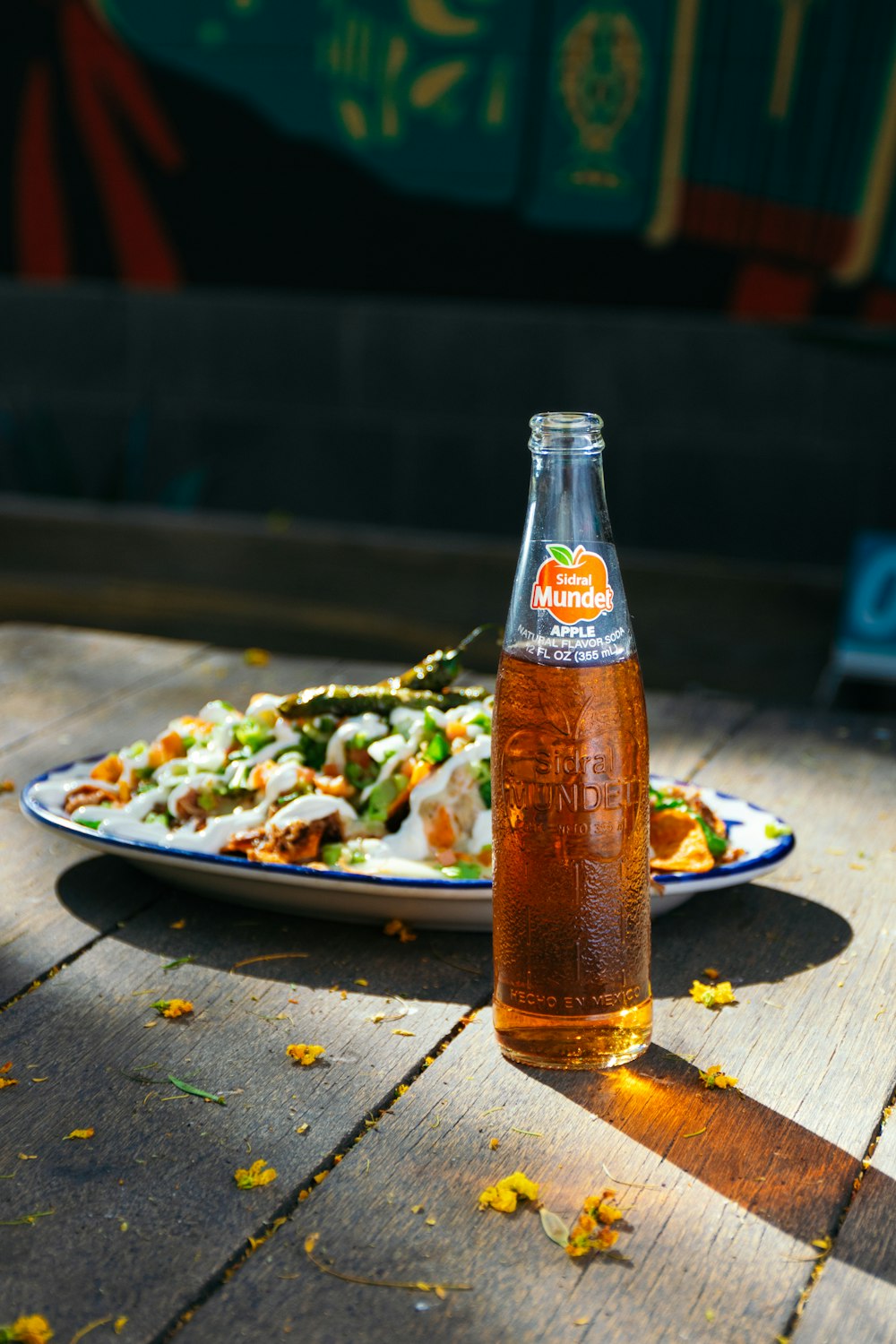 una botella de refresco encima de una mesa junto a un plato de comida