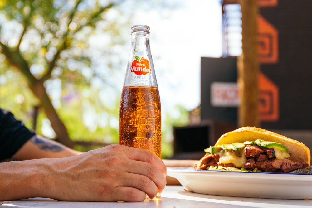 a person sitting at a table with a plate of food and a bottle of soda