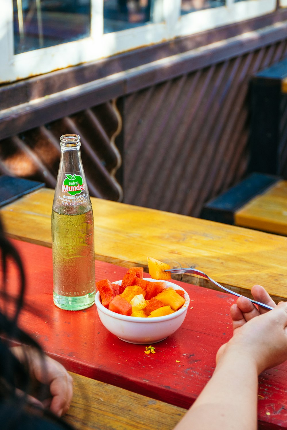 une personne assise à une table avec un bol de fruits et une bouteille de soda