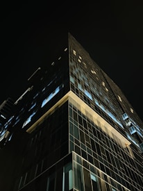 A nighttime view of a high-end corporate glass building illuminated against a black sky.