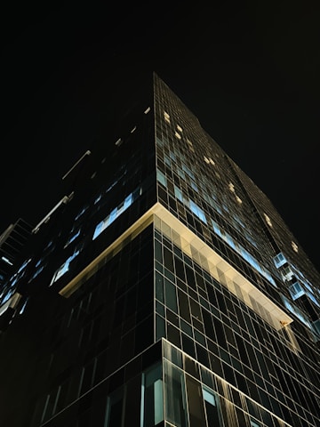 A nighttime view of a high-end corporate glass building illuminated against a black sky.