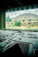 A detailed architectural model is displayed in the foreground, representing a complex of ancient structures and layout. Large windows in the background reveal a pyramid and natural landscape with trees and shrubs, bathed in daylight.