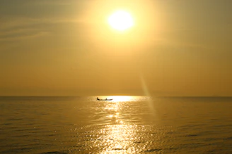 A serene boat gliding over calm blue waters under a golden sunset.