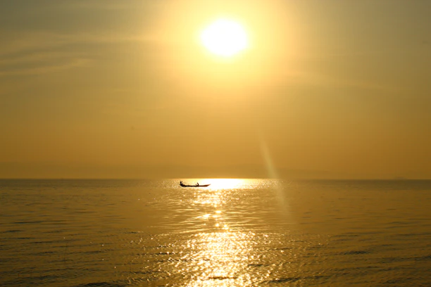 A serene boat gliding over calm blue waters under a golden sunset.