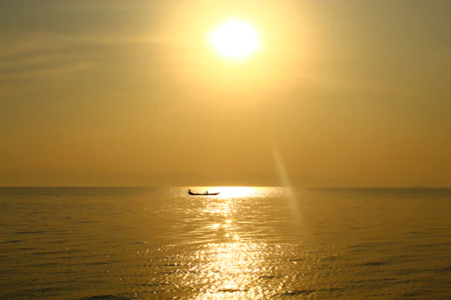 A sun-drenched boat gently cutting through calm waters, silhouetted by a golden sunset.