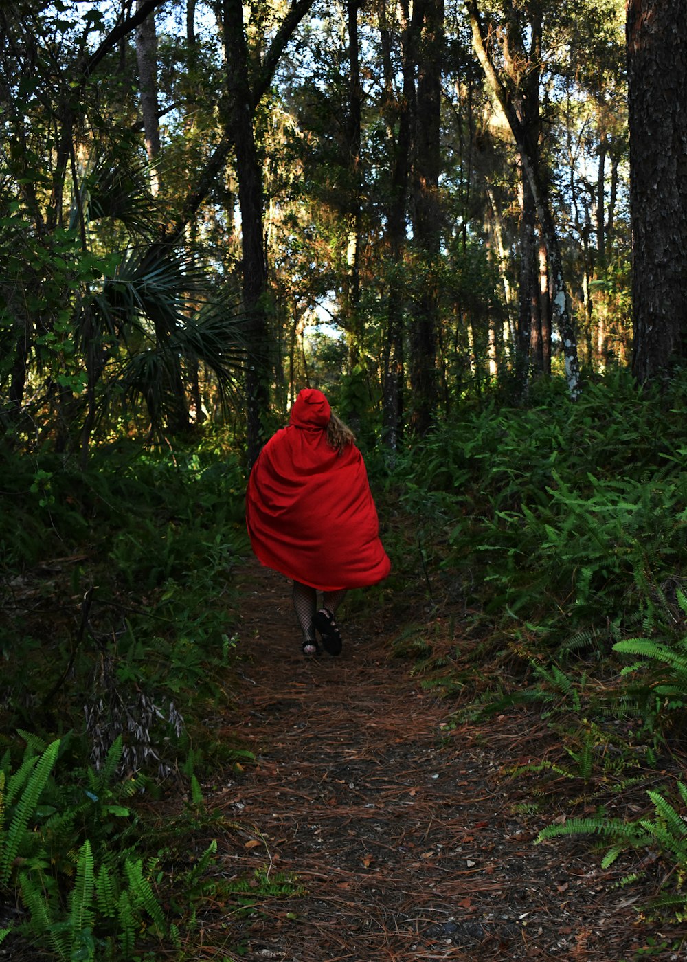 a woman in a red cape is walking through the woods