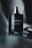 A dark, elegant perfume bottle stands upright, adorned with water droplets. The bottle features the words 'Sauvage' and 'Dior' in sleek, reflective lettering. A blurred, moody background adds to the sophisticated and luxurious vibe.