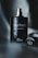 A dark, elegant perfume bottle stands upright, adorned with water droplets. The bottle features the words 'Sauvage' and 'Dior' in sleek, reflective lettering. A blurred, moody background adds to the sophisticated and luxurious vibe.