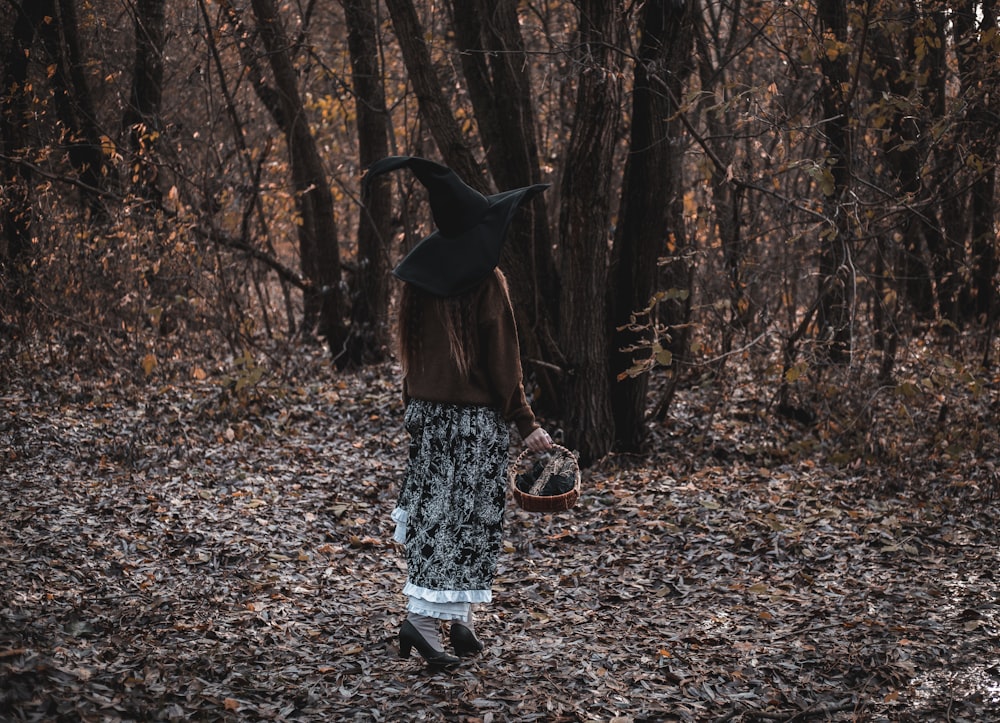 a woman in a witches hat walking through a forest