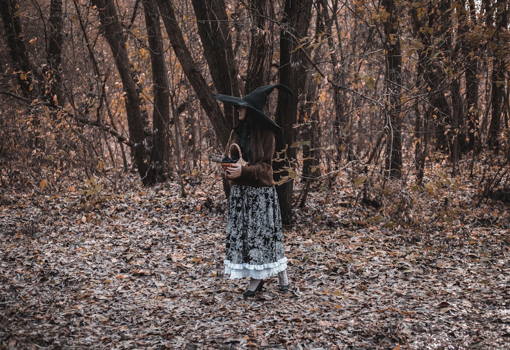 魔女の衣装を着た女性が森の中に立つ
