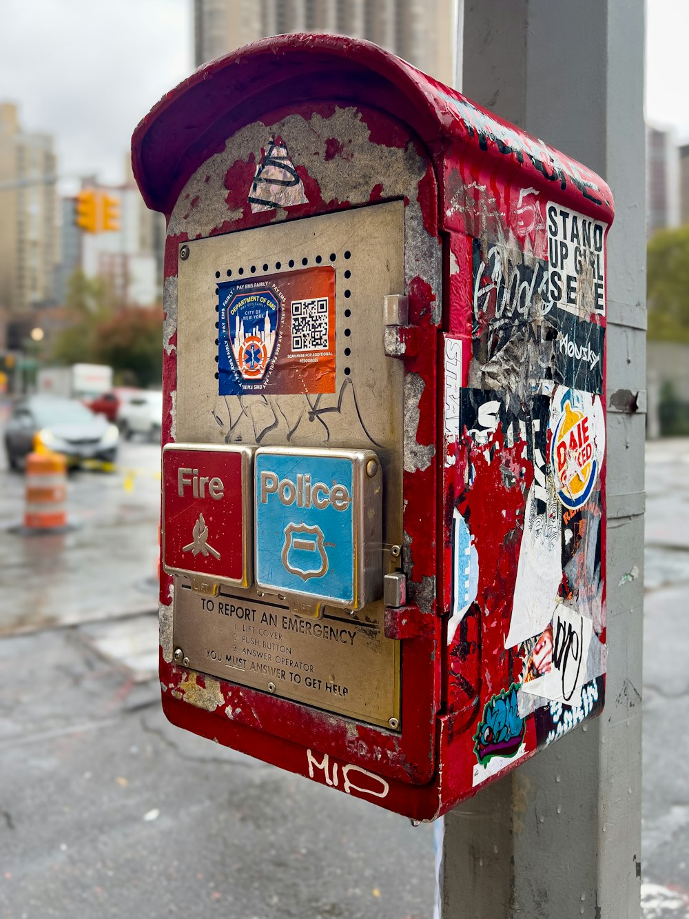 a red mailbox covered in stickers on a city street