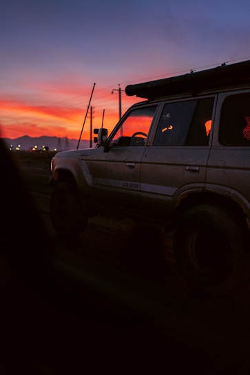 A vibrant jeep climbing a rugged trail at sunrise with Mount Batur glowing in the background.