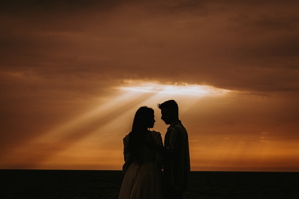 a man and a woman standing in front of a sunset