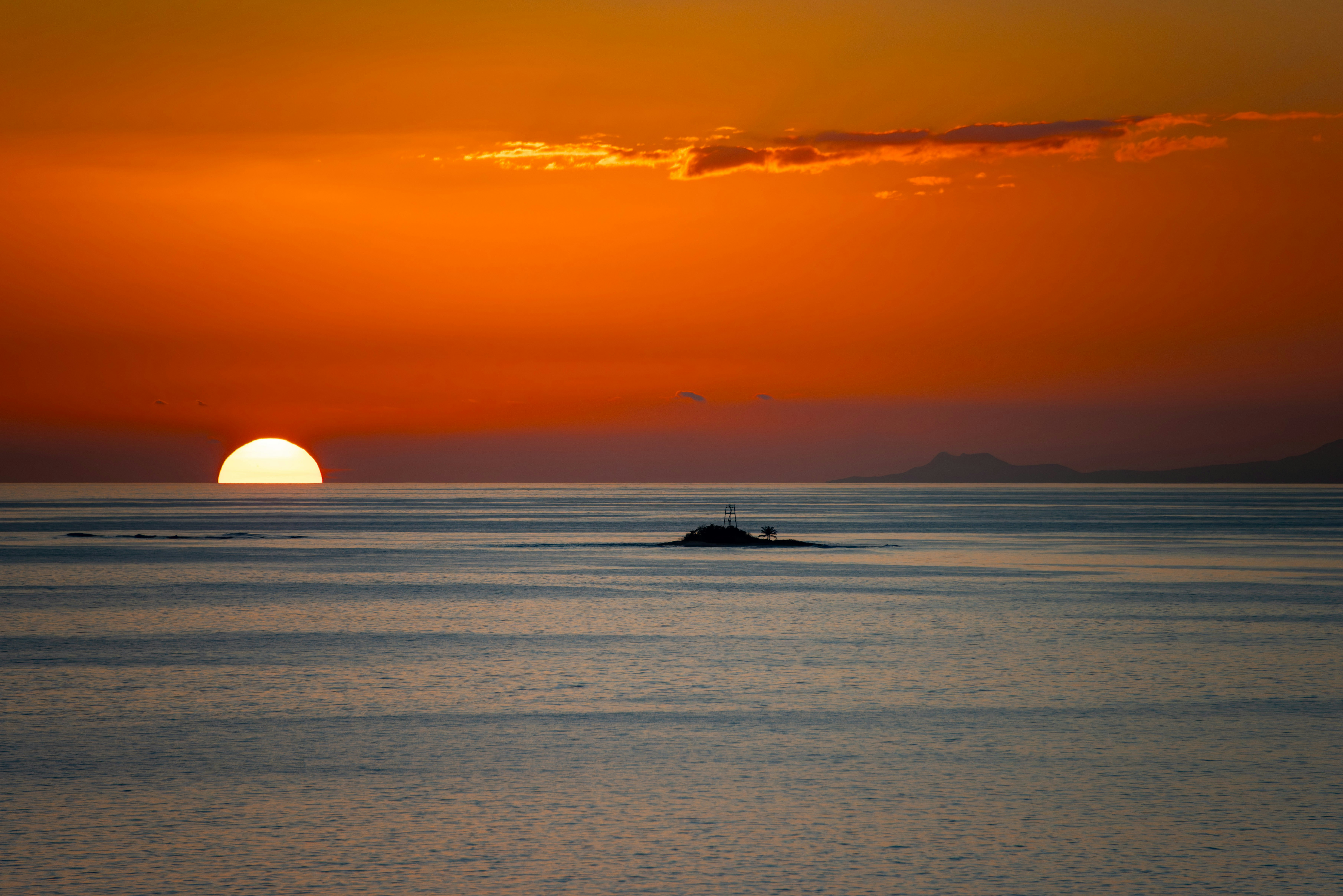 a large body of water with a sunset in the background, Sunset while sailing past a small island out of Antigua in the Caribbean