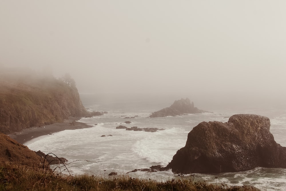 a foggy day at the coast with rocks in the foreground
