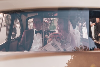 Bride and groom stepping out of a vintage wedding car decorated with white and gold flowers.