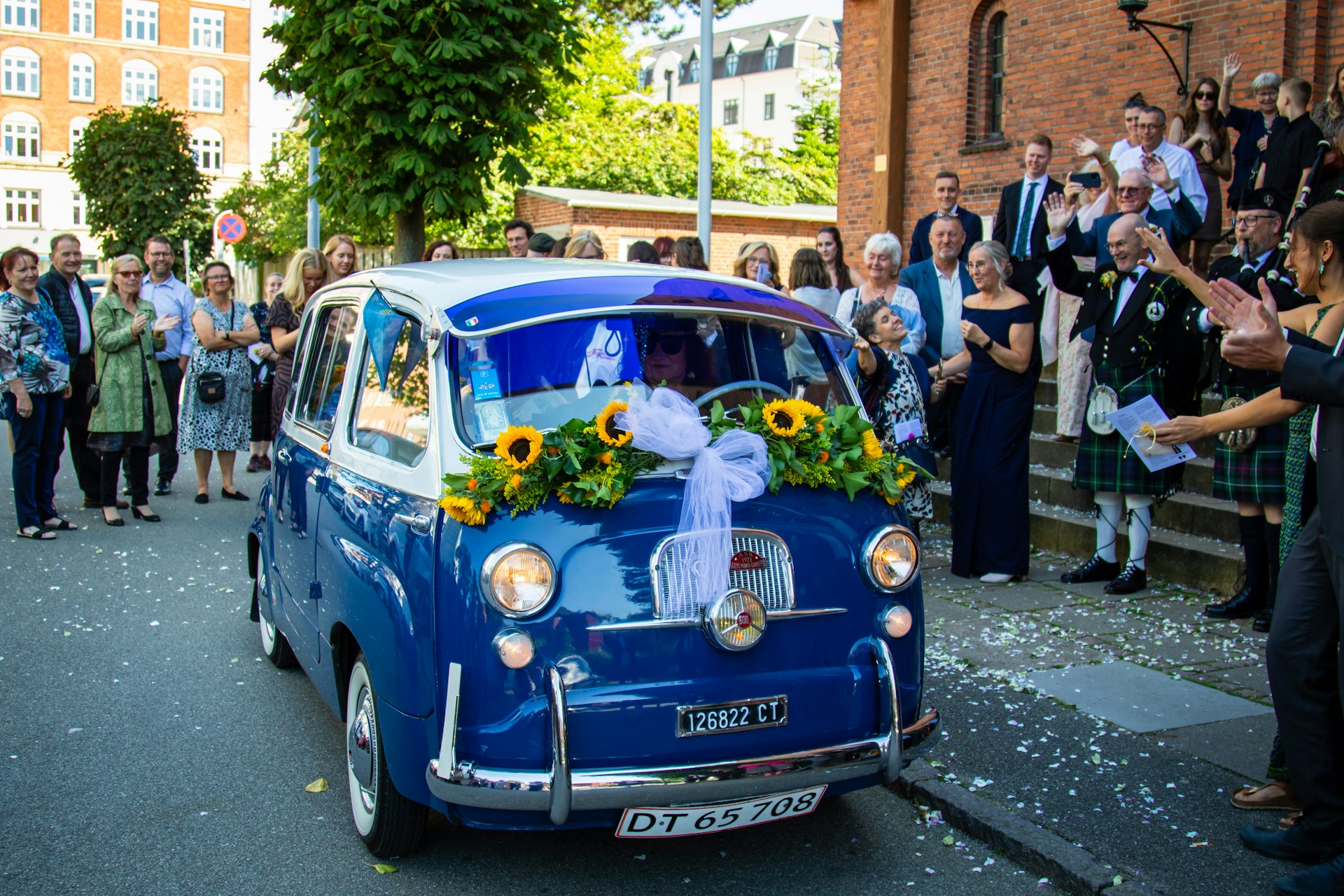 A vintage car decorated with flowers arriving at a vibrant house party in Delhi, with the band and dhol ready to perform.