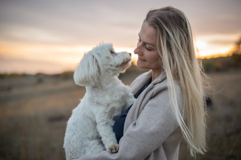 a woman holding a white dog in a field