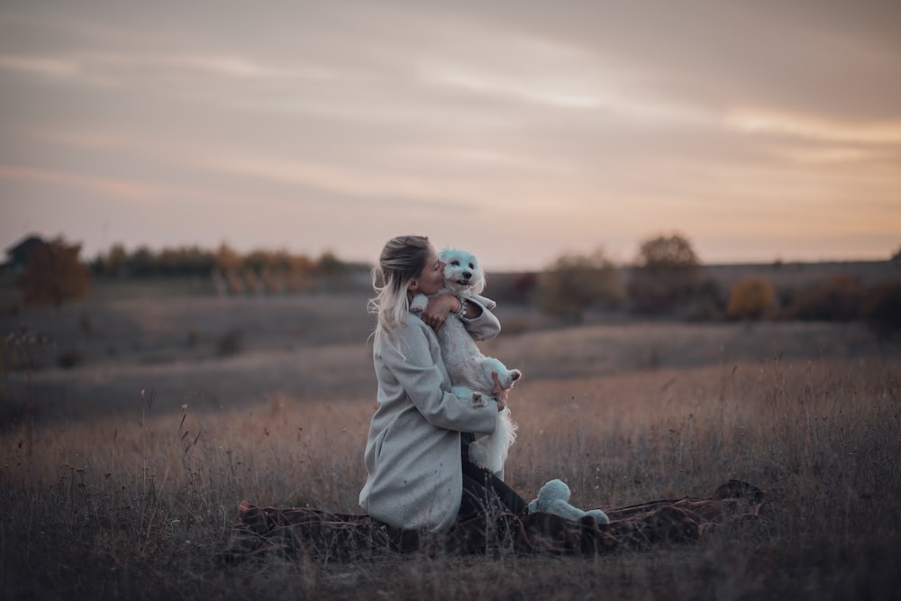 a woman sitting in a field holding a teddy bear