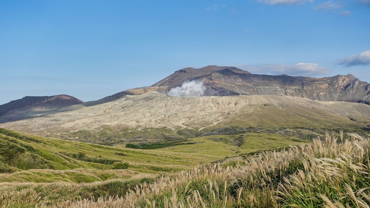 九州阿蘇火山口冒著白煙，前方是連綿的芒草草原