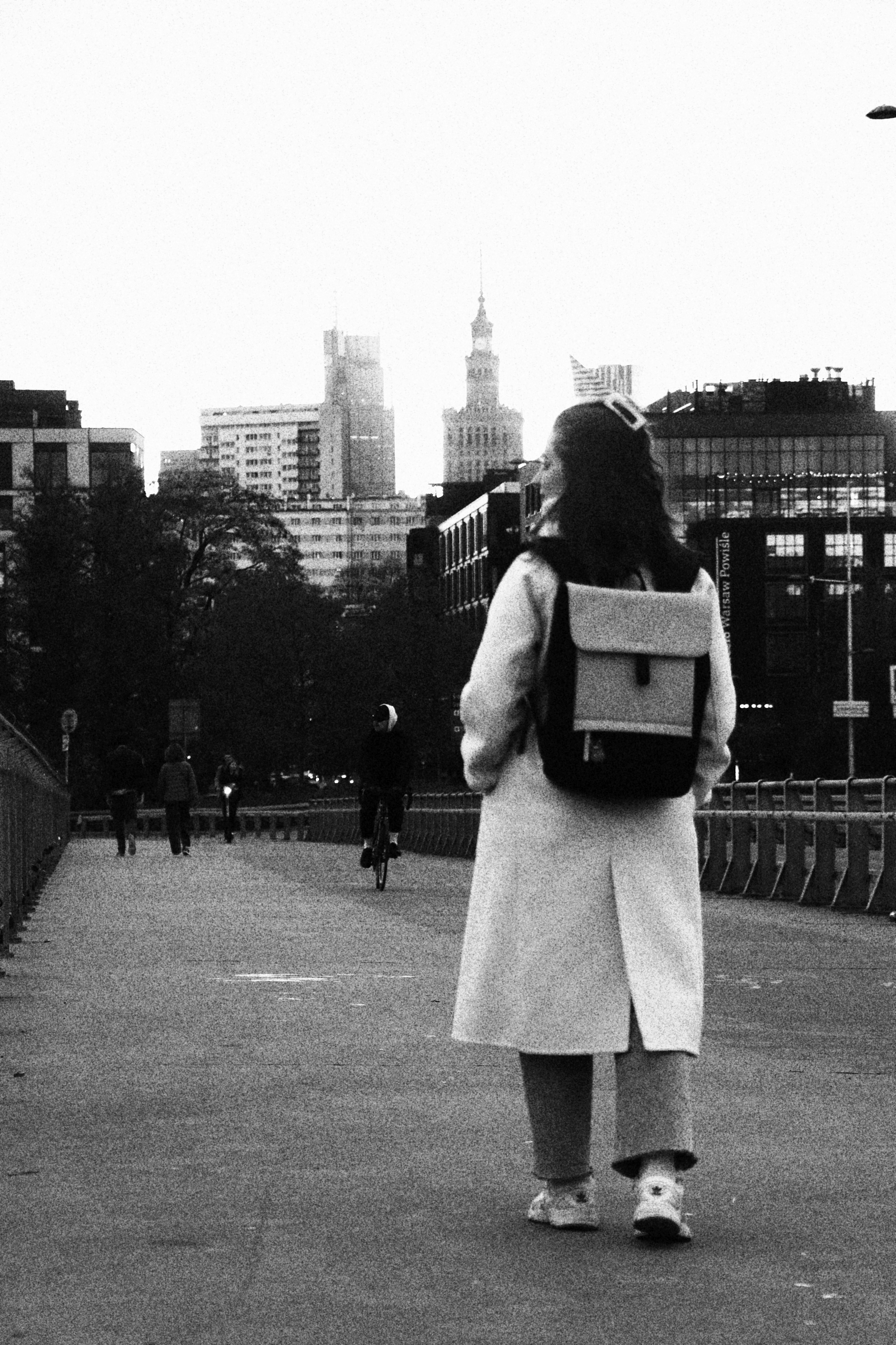 a woman walking across a bridge carrying a laptop