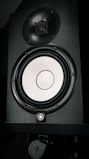 A black speaker with a shiny, silver-colored woofer and a smaller tweeter located above it. The speaker features a logo and appears to be mounted on a stand.