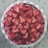 A round dessert garnished generously with sliced strawberries on a cream-like layer, set within a white ceramic pie dish on a marble countertop.