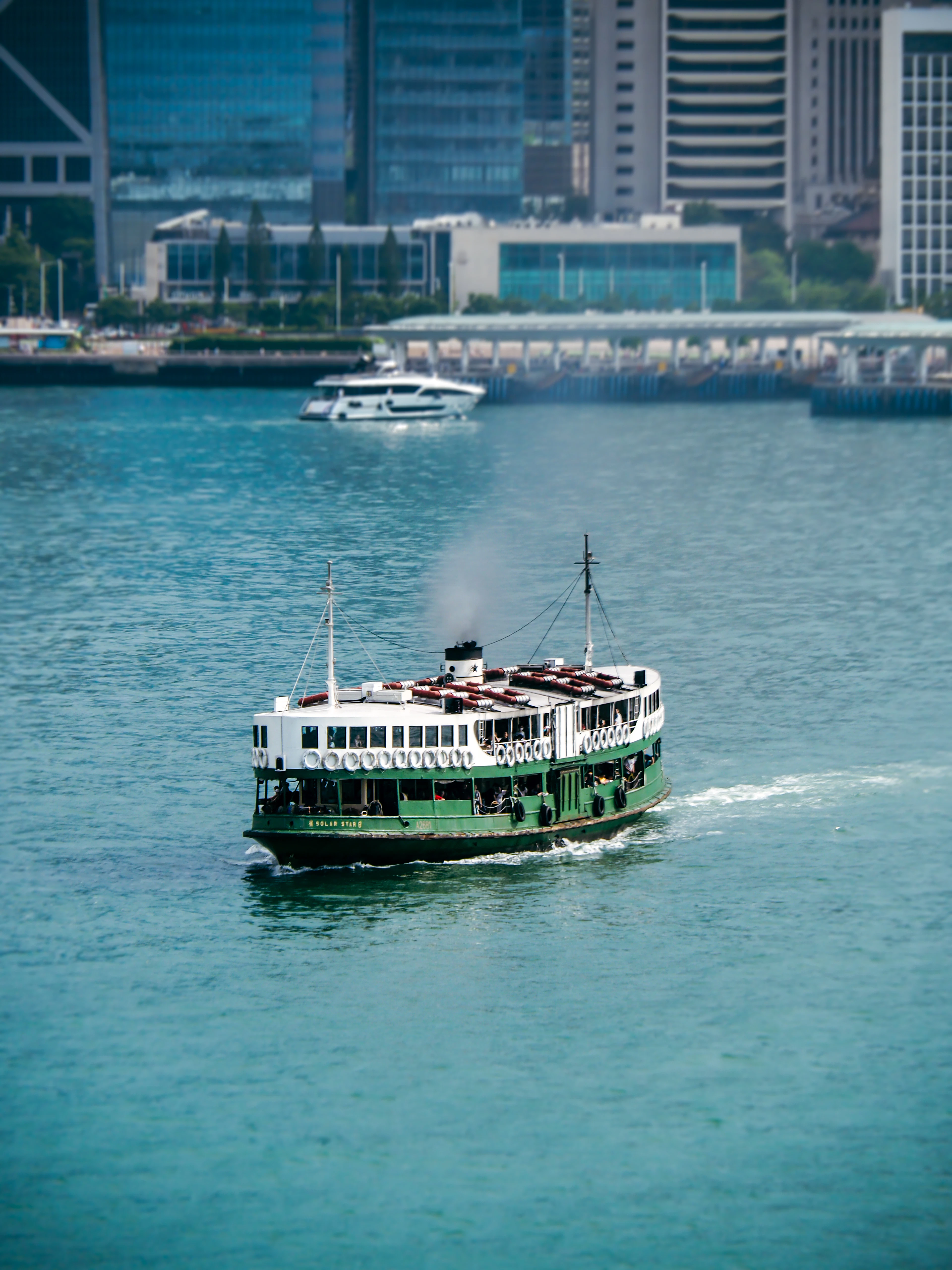 A green and white Star Ferry crossing the turquoise water of Victoria Harbour with Hong Kong's Central waterfront behind
