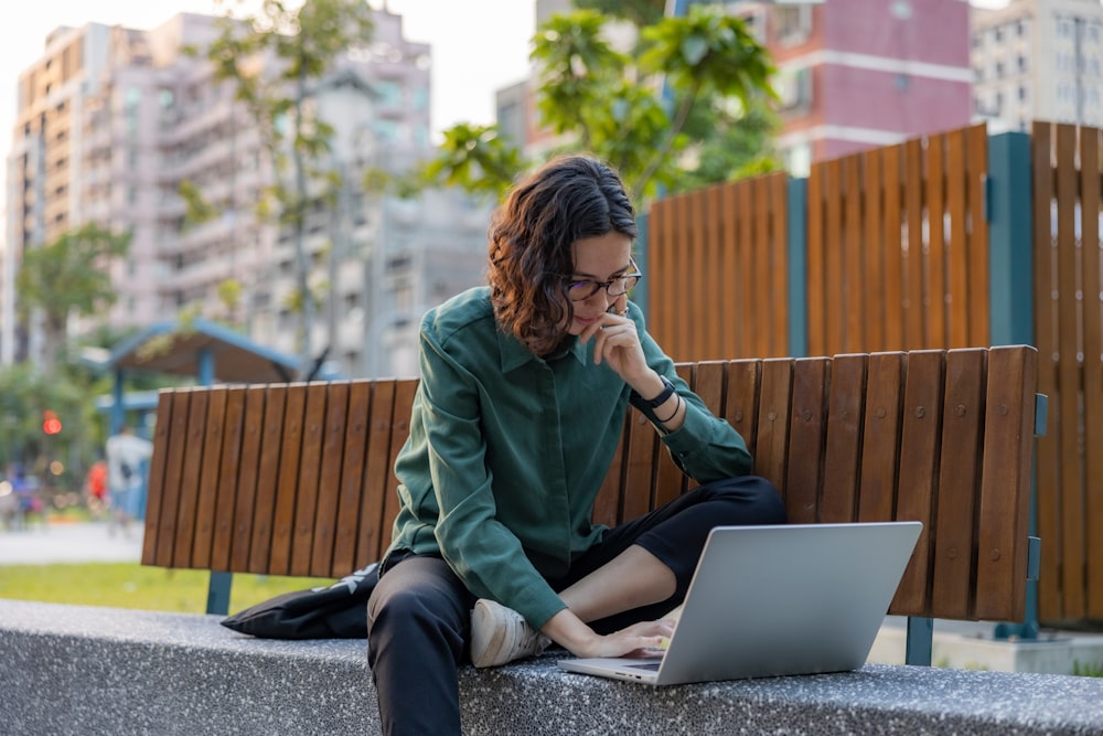 a woman sitting on a bench using a laptop computer