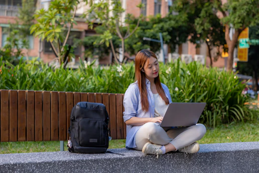 A thoughtful student sitting cross-legged on a campus bench, laptop open, researching internships.