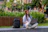 Happy young man with a backpack, sitting outdoors with a laptop and study materials.