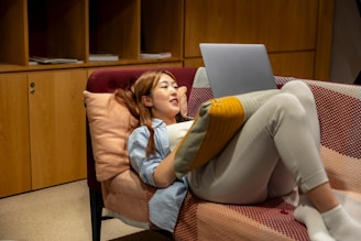 A person relaxing on a sofa with a laptop, enjoying a popular international movie.