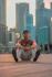 a man sitting on the ground in front of a city skyline