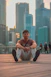 a man sitting on the ground in front of a city skyline