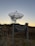 A large satellite dish set against a twilight sky with a sign in the foreground reading '400 - Reservoir Road Authorized Access Only No Trespassing.' The ground is covered in dry grass, and there is a fence surrounding the area.