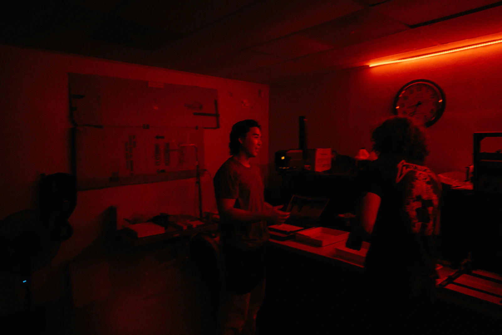 Two people working through clues in a dim, red-lit escape room