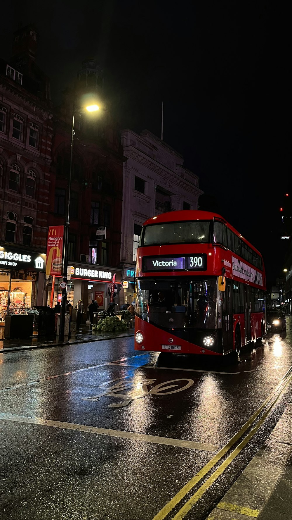 a red double decker bus driving down a street at night