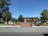A well-maintained public square with a red brick path leads to a fountain in front of a two-story building labeled 'Union Bank.' The area is surrounded by trees and neatly trimmed lawns, with several street lamps and benches. A clear blue sky enhances the peaceful setting.