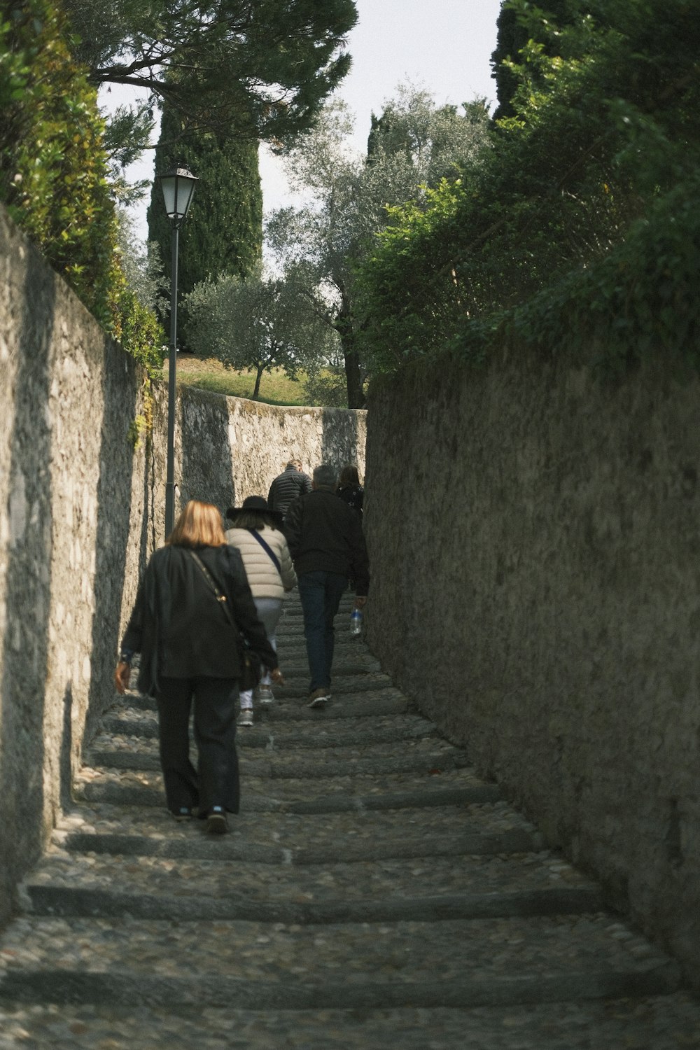 a group of people walking down a street next to a stone wall